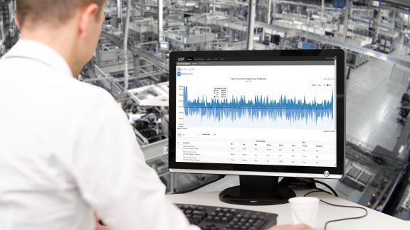 Person reviewing factory floor performance data on a screen while looking out over the production floor