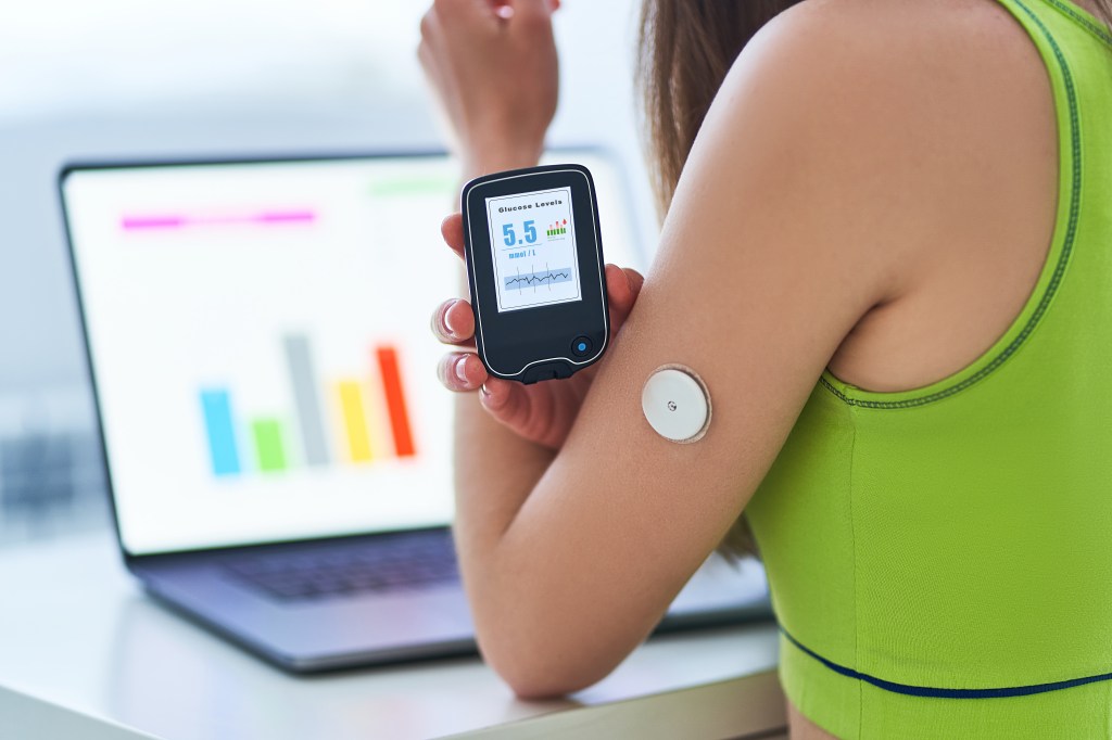 Person holding glucose meter close to wearable glucose monitor on back of arm