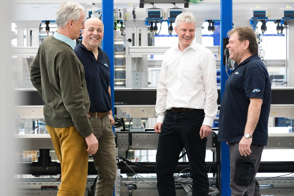 Vier männliche Kollegen stehen neben einer Maschine und haben gemeinsam Spaß