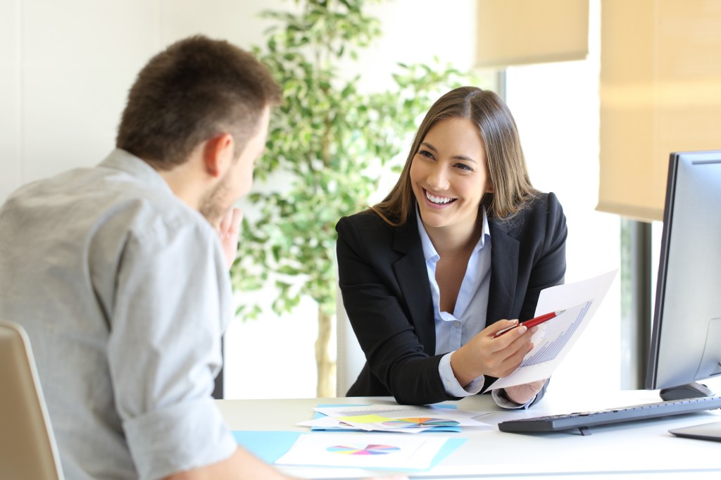 A male and female employee discuss work across a meeting table