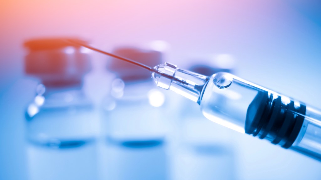 Glass syringe with blurred glass vials in the background